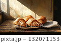 Morning light highlights freshly baked croissants on a wooden table. Warm crusts and soft shadows create a cozy breakfast mood.	 132071153