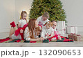 Family on cozy blanket by beautifully decorated Christmas tree. 132090653