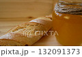 A jar of golden sweet honey on the table, next to a baguette and a wooden spoon 132091373