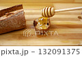 Golden honey drips from a wooden spoon onto a piece of rye bread.  132091375