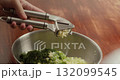 Close-up of a cook's hands pressing garlic cloves into a special garlic press to prepare a filling for baked goods. Chopping garlic into a container with dill and green onions. 132099545