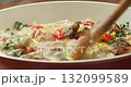 Chef cooks tomatoes, spinach, and salmon in creamy sauce, stirring with a wooden spatula. 4K close-up of home cooking process. 132099589