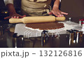 A close-up shot of hands using a wooden rolling pin to flatten brown dough on a floured surface. Perfect for depicting homemade baking, holiday preparations, or culinary arts. 132126816