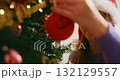 Woman Decorating Christmas Tree with Ornaments and Santa Hat 132129557