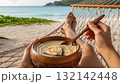 Person relaxing in hammock on tropical beach eating delicious vanilla dessert from wooden bowl 132142448