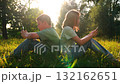 Kids on smartphones in sunny park, Boy and girl back to back on phones, Children using mobile devices outdoors, Summer meadow screen time concept, Digital kids in nature at sunset, Friends scrolling 132162651