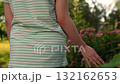 gentle hand touching green leaves at golden hour, hand gliding through lush garden foliage in summer, close-up of hand brushing leaves with pink blossoms, striped shirt arm exploring fresh garden 132162653