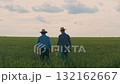 Two farmers walking in a green wheat field, Farmers inspecting crops together, Agricultural teamwork in the countryside, Rural scene with farmers and crops, Field workers discussing harvest 132162667