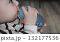 Baby holding gray bottle on wooden floor 132177536