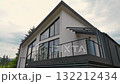 Minimalist modern cottage with a tall pitched roof, large window facade, and spacious deck against a cloudy sky 132212434