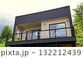 Modern cubic minimalist house exterior with dark metal siding and large glass windows overlooking a natural landscape 132212439