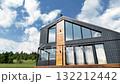 Contemporary two-story house with dark cladding and light wood accents set against a bright blue sky with clouds 132212442