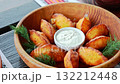 Golden roasted potato wedges served with sour cream and fresh dill in a rustic wooden bowl, delicious meal 132212448
