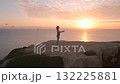 A Tranquil Meditation Moment: A Woman Practicing Yoga at Sunrise on a Cliff Overlooking the Ocean, Embracing Serenity and Nature's Beauty. 132225881
