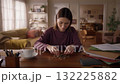 A Young Woman Contemplates Finances While Sorting Coins at Her Home Workspace, Reflecting on Budgeting, Savings, and Financial Planning in a Cozy Setting. 132225882