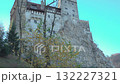 Historic Bran Castle, Romania low angle day exterior, perched on a rocky cliff surrounded by trees under a clear blue sky. 132227321