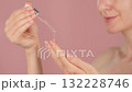Pipette of serum in the hands of a young woman with radiant skin. Macro close-up drops of serum dripped from the dropper. Beauty routine on a pink background. Slow motion. Cosmetic concept ads 132228746