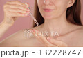 Young woman holding a dropper with serum. Drops fallling from a glass pipette. Macro close-up view. Pink background. Beauty, Cosmetology, Spa ads. Liquid collagen skincare product, beauty concept 132228747