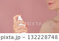 Elegant close-up of a woman applying a facial mist, holding the spray bottle near her face, fine water droplets visible in the air. Unrecognizable woman spraying a moisturizing facial mist on her face 132228748