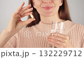 Close-up of an unrecognizable woman holding a a vitamin pill and a glass of water, smiling before taking the pill. Concept of daily health and wellness routine. 132229712