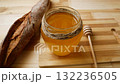 jar of fresh golden honey, next to a bread baguette and a wooden spoon for honey 132236505