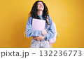 Happy student holding books and celebrating on yellow background 132236773