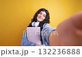 Student taking a selfie with headphones and notebook on yellow background 132236888