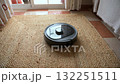 A sleek robot vacuum cleaner waits patiently on a textured jute rug, symbolizing modern household automation and smart living. This innovative device offers convenient and efficient cleaning solutions 132251511
