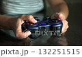 A person's hands skillfully press buttons and move joysticks on a dark blue game controller, enjoying a video game. The focus is on the interactive experience and modern entertainment. 132251515
