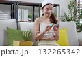 Young asian woman sitting on sofa choice cosmetic cream or lotion with shopping online. 132265342