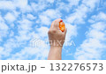 Hand raising orange translucent water balloon into blue sky 132276573