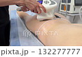 young woman performs an infrared wellness massage on the buttocks of a client lying on a massage table in a bright spa room promoting relaxation, body care, and rejuvenation during the session. 132277777