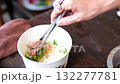 Traditional Vietnamese street food preparation showing a local vendor making hot noodle soup with meat and rice noodles in a paper bowl filled with boiling water in an authentic Asian market. 132277781