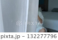 Mature blonde woman in bathrobe applying hand cream, sitting on chair in bedroom, sunlight through curtain 132277796