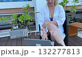 Adult European woman in blue swimsuit and robe working online by pool with laptop and headphones, remote work and summer relaxation lifestyle 132277813