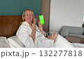 Happy mature woman in glasses under blanket dancing and smiling, showing smartphone with green screen chroma key, concept for advertising or social media content 132277818