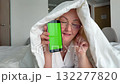 Happy mature woman in glasses under blanket dancing and smiling, showing smartphone with green screen chroma key, concept for advertising or social media content 132277820