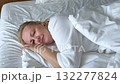 A woman peacefully sleeping in bed with white sheets. The image captures a serene and restful moment in a cozy bedroom setting. Ideal for concepts of relaxation, sleep, and comfort. 132277824