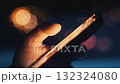 Close up of hand holding and using smartphone at night, with blurred city lights creating bokeh effect in background, suggesting connection and communication in urban environment 132324080