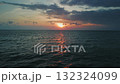 Sun setting over tranquil ocean, casting warm golden glow across water surface, while dramatic clouds fill sky, enhancing picturesque evening atmosphere. Sun peeking above calm sea horizon 132324099