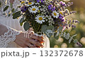 A close-up of a bride in a beautiful white lace dress holding a rustic wedding bouquet 132372678