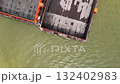 Aerial view of an industrial port with several large barges one featuring a bright orange edge surrounded by cranes and buildings for cargo operations 132402983