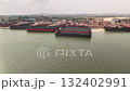 Aerial view of an industrial port with several large barges one featuring a bright orange edge surrounded by cranes and buildings for cargo operations 132402991