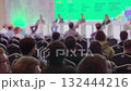 Conference audience listens to panel discussion on stage with green backdrop 132444216