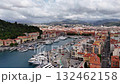 Aerial view of the harbor in Nice, France with yachts, colorful Mediterranean buildings, and green hills under a cloudy sky. 132462158