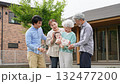 A three-generation family smiling and surrounding a baby in front of their house 132477200