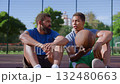 Portrait of attractive athletic fit African American male basketball players with ball enjoying leisure, friendly chatting and sharing while sitting on outdoor court after streetball game in morning. Portrait of attractive athletic fit African American male basketball players with ball enjoying leisure, friendly chatting and sharing while sitting on outdoor court after streetball game in morning. 132480663