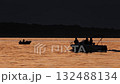 Fisherman sitting in a boat on the sea in orange sunset lights while a motorboat passing by. Fishing from a boat near the coast. Mediterranean scenery with mountains in the background. 132488134