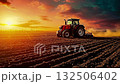 A tractor plowing a field at sunset 132506402
