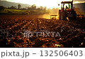 A tractor plowing a field at sunset 132506403
